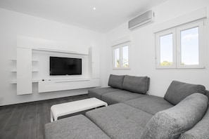 A modern living room with a grey sofa, a white coffee table, a mounted TV, and a window with a view.
