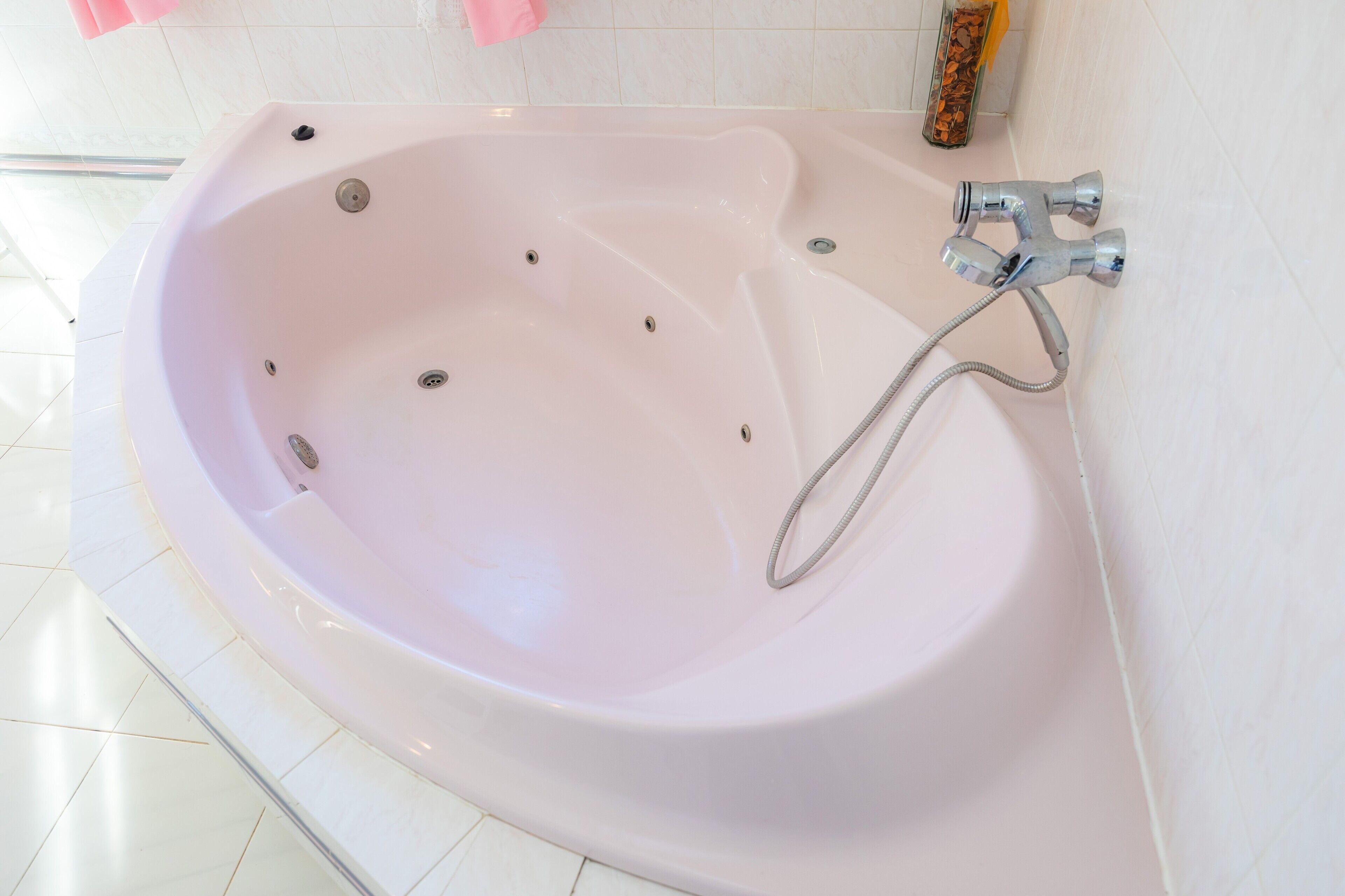 A white bathtub with a shower head and controls, a glass shower door, and a tiled floor.