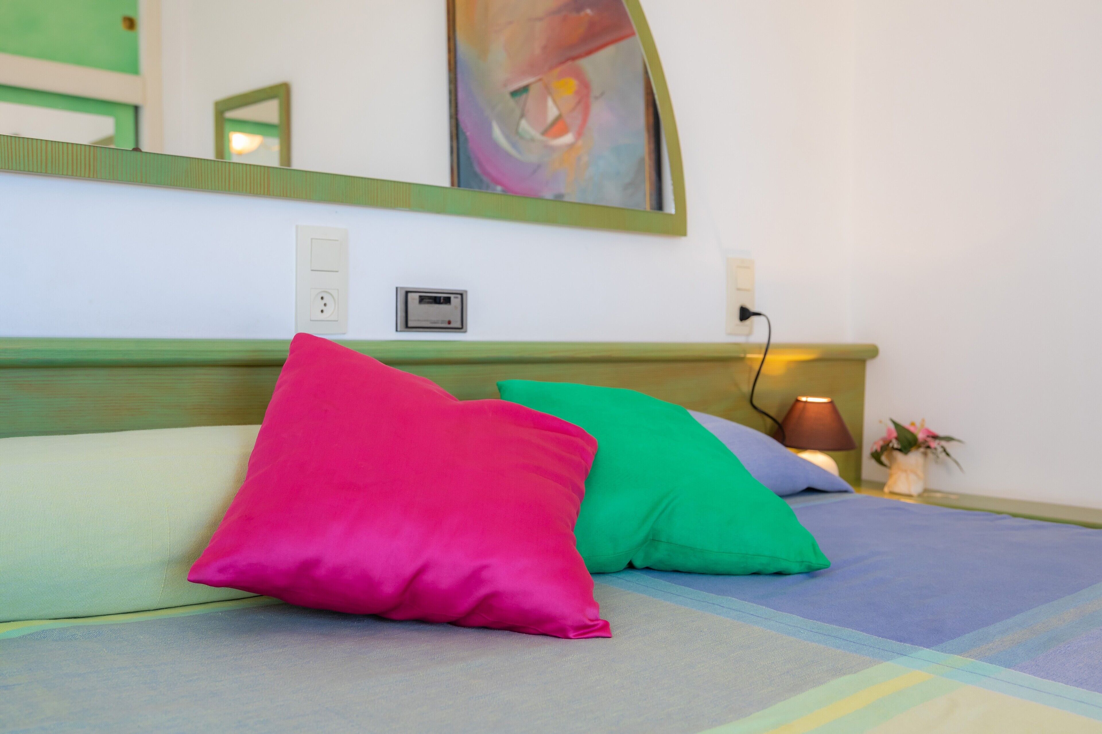 Una cama con almohadas coloridas, una lámpara de noche y un enchufe en la pared.