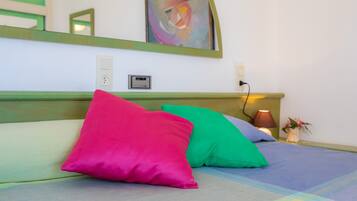 Una cama con almohadas coloridas, una lámpara de noche y un enchufe en la pared.