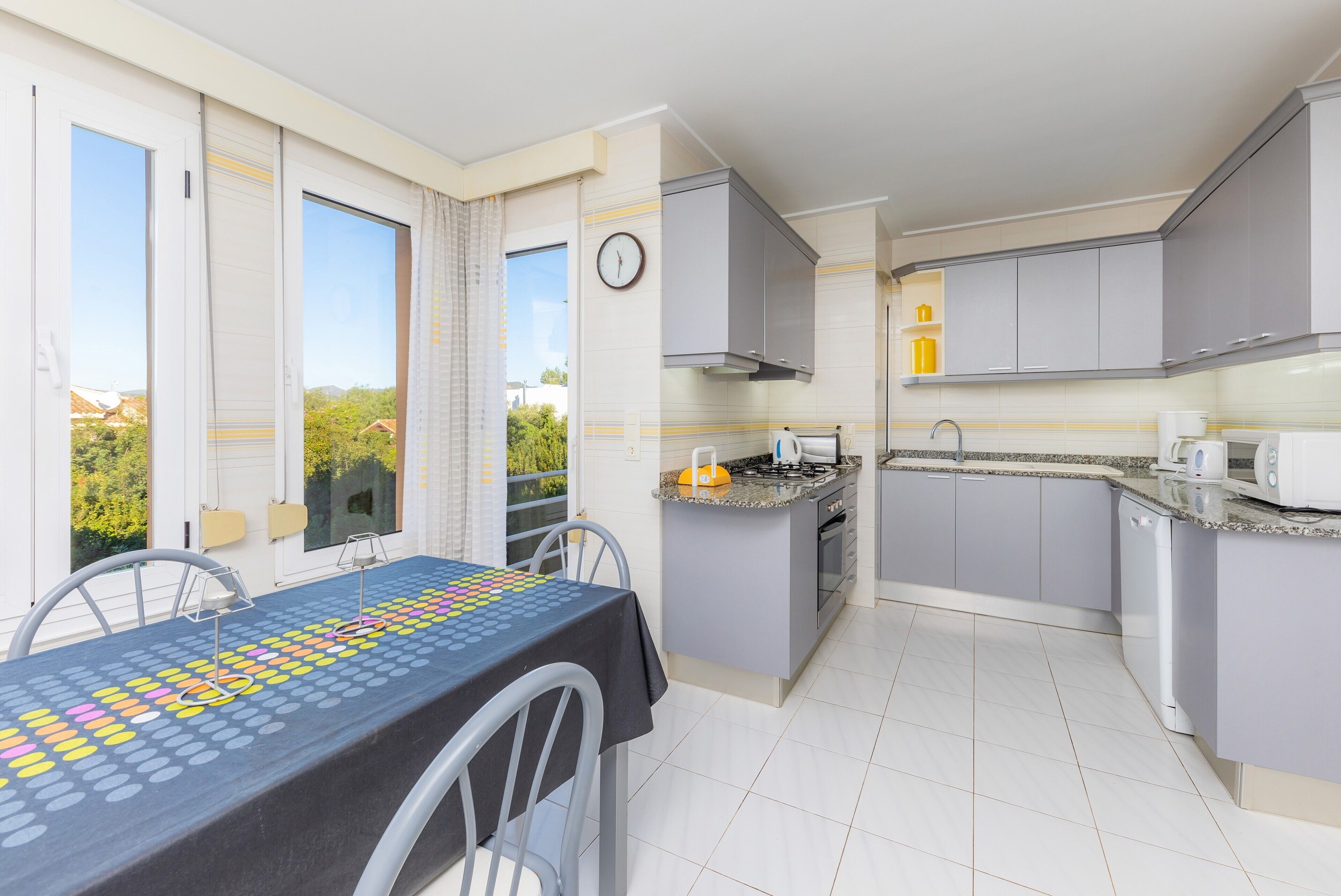 Una cocina moderna con armarios grises, una mesa de comedor con un juego de mesa y vistas al exterior.