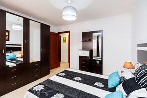 A bedroom with a bed, a wardrobe, a dresser, a mirror, and a door leading to another room.