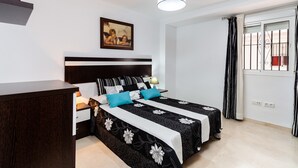 Un dormitorio con cama, mesitas de noche, una lámpara de noche, un cuadro, una ventana con cortinas e iluminación en el techo.
