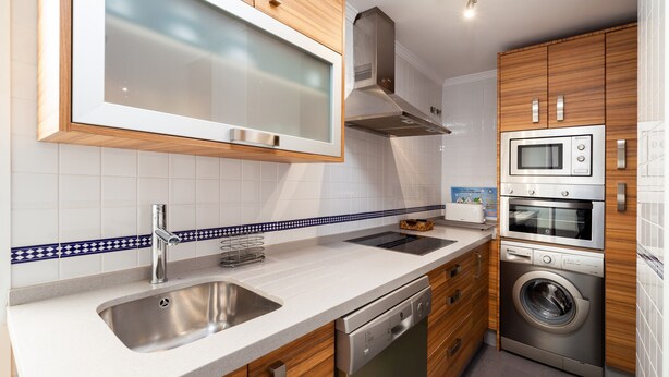 Una cocina moderna con un lavamanos de acero inoxidable, armarios de madera, un microondas, un horno y un lavavajillas.