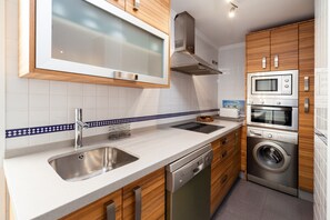 A modern kitchen with a stainless steel sink, wooden cabinets, a microwave, an oven, and a dishwasher.