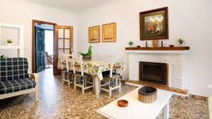 Un salon avec une cheminée, une table à manger avec des chaises, un canapé et un luminaire au plafond.