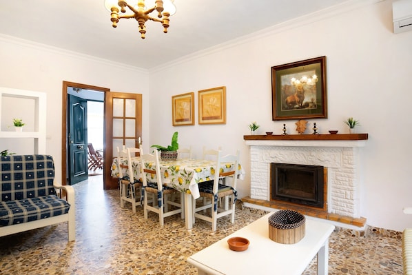 A living room with a fireplace, a dining table with chairs, a sofa, and a ceiling light fixture.