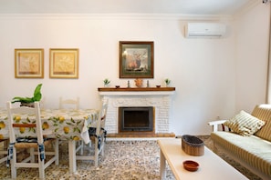A living room with a fireplace, a dining table with chairs, a sofa, and two framed pictures on the wall.