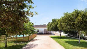 Un chemin menant à un bâtiment doté d’une piscine, entouré d’arbres et d’une clôture en bois.