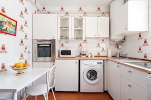 Een kleine keuken met een magnetron, oven, wasmachine en een spoelbak.