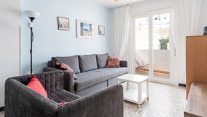 A living room with a grey sofa, a red armchair, a white coffee table, a ceiling fan, and a view through a glass door.