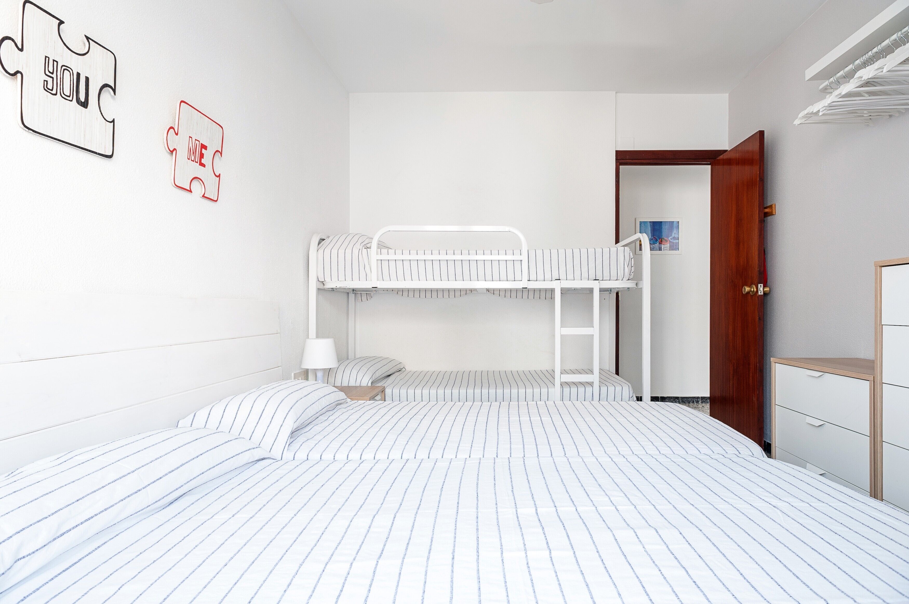 A bunk bed room with striped bedding, a wooden door, and a wall-mounted puzzle piece decoration.