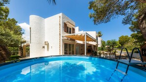 Una piscina con escalera, un edificio de fachada blanca y follaje circundante.