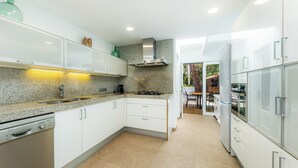 Una cocina moderna con armarios blancos, encimeras de granito, lavavajillas, estufa y campana extractora de acero inoxidable.