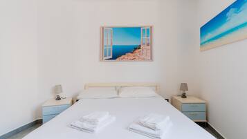 Ein Schlafzimmer mit einem Bett, zwei Nachttischen, einem Strandbild und Blick aufs Meer.