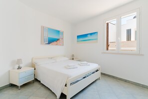 A bedroom with a bed, nightstands, a window with an open door, and two wall-mounted pictures.