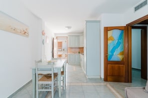 A modern kitchen with white cabinets, a dining area with a table and chairs, and a wooden door with a stained glass panel.