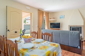 A dining area with a table set for two, a sofa, a television, and a fireplace.