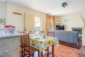 A dining area with a table set for two, a TV, and a sofa in the background.