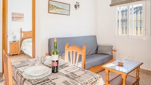 A room with a dining table set for two, a bottle of wine, a grey sofa, and a small table with a bowl. - Air-Conditioned Apartment Close to the Beach with Pool, Terrace, Garden & Wi-Fi (Zahora)