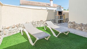 A patio with two lounge chairs, a stone wall, and a barbecue grill. - Air-Conditioned Apartment Close to the Beach with Pool, Terrace, Garden & Wi-Fi (Zahora)