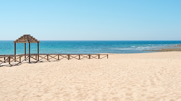 Ein Strand mit einer Holzkonstruktion, blauem Himmel und ruhiger See.