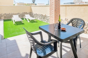 Eine Terrasse mit Tisch, Stühlen, einer Weinflasche und einer Schale.