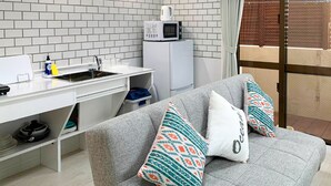Un espacio habitable compacto con kitchenette, sofá gris con cojines estampados y vistas a través de una puerta corrediza de vidrio.