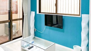 Un baño moderno con cabina de ducha de vidrio, un televisor montado y una mesita de cristal con artículos de aseo.