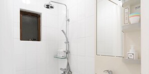 A modern bathroom with a shower, a mirror, and a shelf with toiletries. - WARAYUN SO Port city May (Naha)