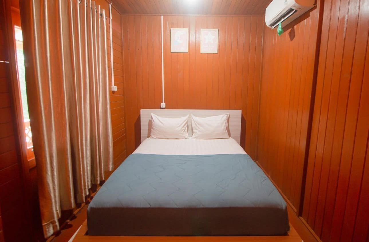 A single bed with a white headboard and pillows, a blue bedspread, and wooden paneling on the walls.