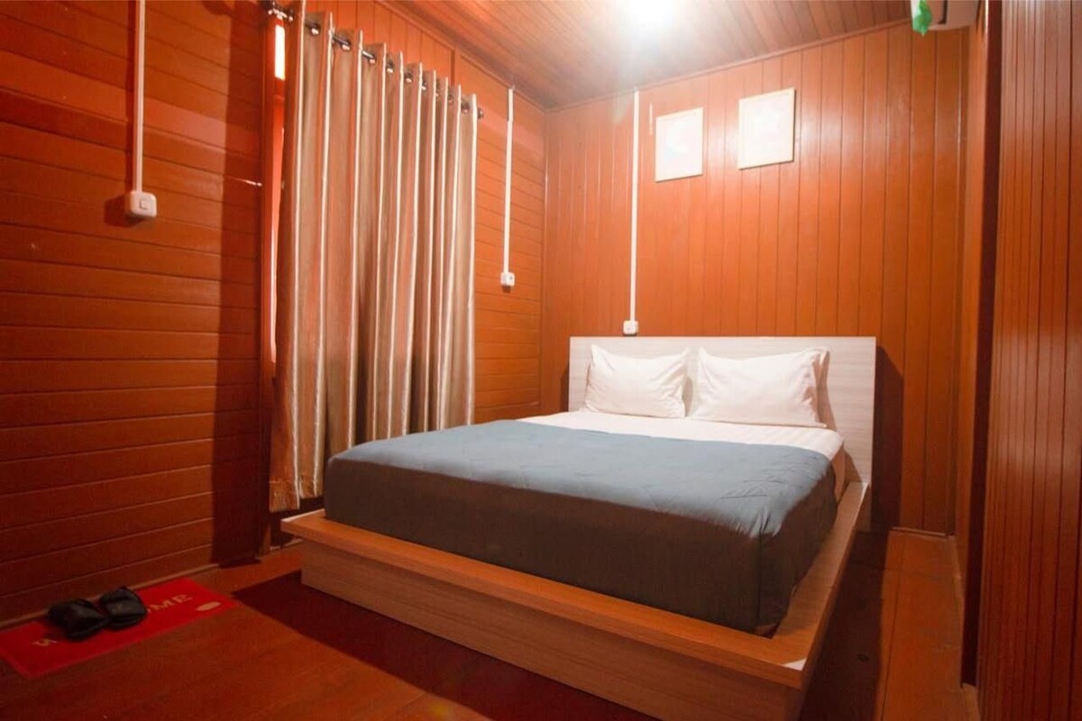A wooden-paneled room with a bed, a red mat, and a white wall-mounted light fixture.