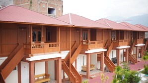 Une rangée de bungalows en bois dotés de balcons et d’escaliers en bois, avec un bâtiment en briques en arrière-plan.