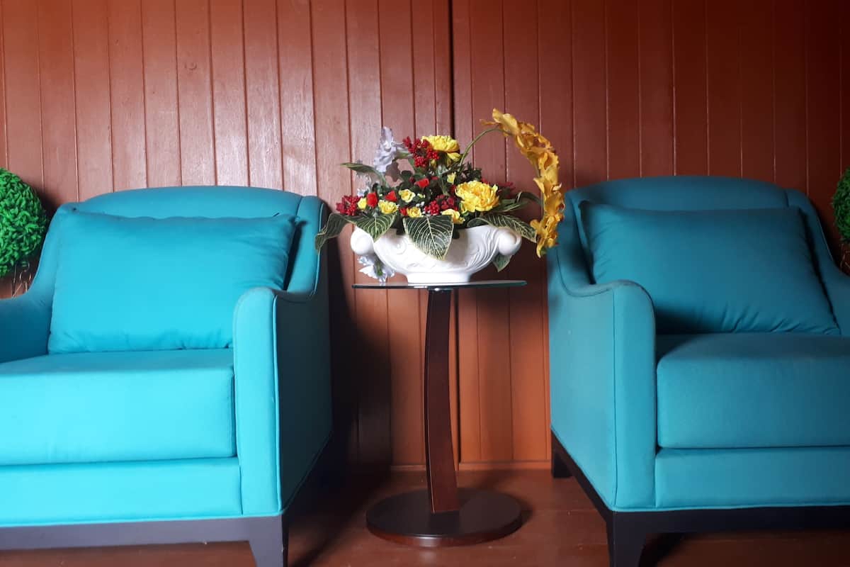 Deux fauteuils turquoise placés face à face, avec une petite table entre eux, un vase décoratif rempli de fleurs et un mur lambrissé.