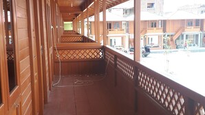 Un couloir couvert aux murs en bois et au toit en métal, qui mène à un balcon d’où l’on peut admirer les bâtiments et les voitures garées.