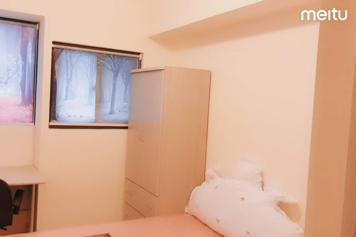 A bedroom with a bed, a desk, a chair, a wardrobe, and a window with a view of trees.