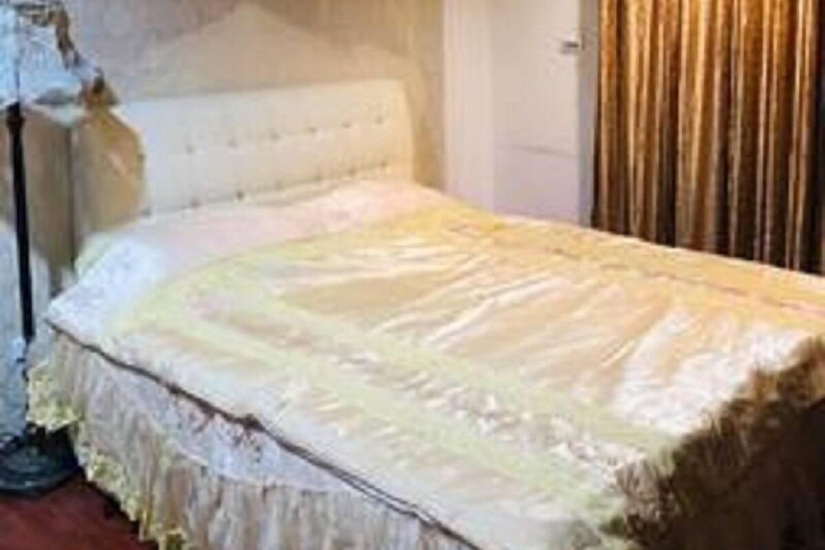 A bedroom with a large bed, a nightstand, a lamp, and a window with curtains.