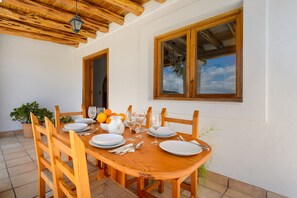 A wooden dining table set for four with white plates, glasses, and cutlery, surrounded by wooden chairs.