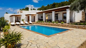 A poolside area with a stone pool, lounge chairs, and a covered patio. - Air-conditioned Villa with Pool, Terrace and Wi-Fi (Sant Joan de Labritja)