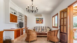 A living room with a sofa, two wicker chairs, a TV, and a painting on the wall. - Air-conditioned Villa with Pool, Terrace and Wi-Fi (Sant Joan de Labritja)