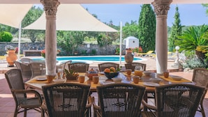 An outdoor dining area with wicker chairs and tables, a pool in the background, and a stone wall with greenery. - Beautiful Holiday Home with Mountain View, Pool, Wi-Fi, Garden and Air Conditioning (Santa Eulalia del Río)