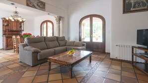 A living room with a sofa, a coffee table with fruit, a wooden cabinet, and a television. - Beautiful Holiday Home with Mountain View, Pool, Wi-Fi, Garden and Air Conditioning (Santa Eulalia del Río)