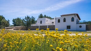 A white building with a balcony, surrounded by yellow flowers and trees. - Beautiful Holiday Home with Mountain View, Pool, Wi-Fi, Garden and Air Conditioning (Santa Eulalia del Río)