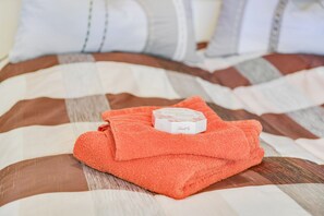 Un letto rifatto con una coperta a righe, un asciugamano arancione piegato e una scatolina sul letto.