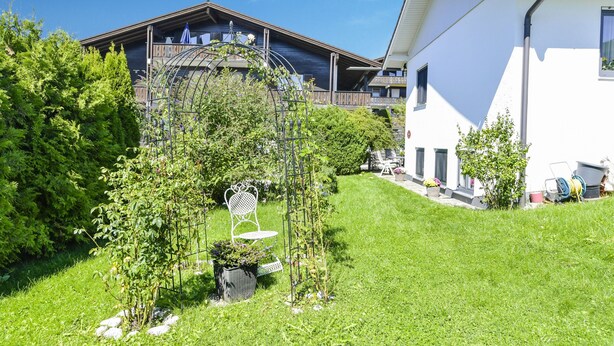 Un edificio residencial con balcón, un jardín con una escultura de metal y una pared exterior blanca.