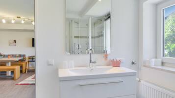 A modern bathroom with a large mirror, white sink, and a window with a view of greenery.
