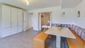 Una habitación moderna con una mesa de comedor de madera, asientos tipo banco, un armario y una cama con cabecero colorido.