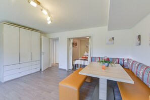 Una habitación moderna con una mesa de comedor de madera, asientos tipo banco, un armario y una cama con cabecero colorido.