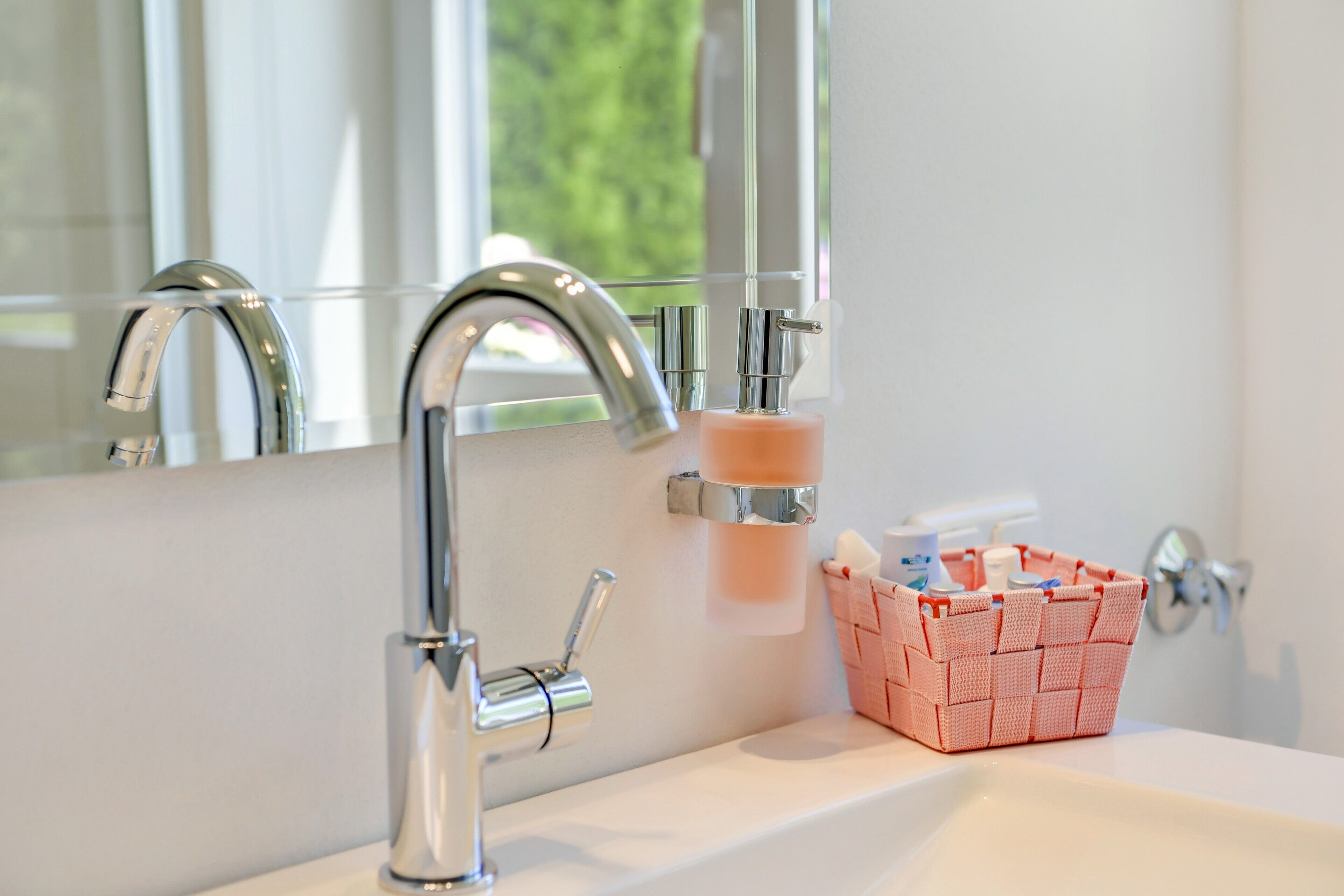 A bathroom with a modern faucet, a soap dispenser, and a basket of toiletries.