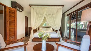 A bedroom with a canopy bed, a sitting area with chairs, a small table, and a vase of flowers.